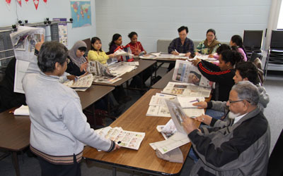 teacher and adult students looking at newspapers